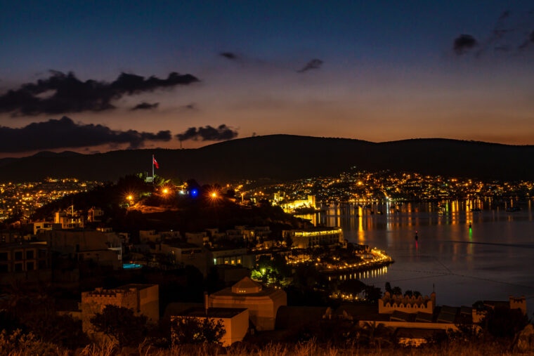 A bird's-eye view of Bodrum. It's nighttime, and the town is surrounded by nothing but yellow lights and white houses.