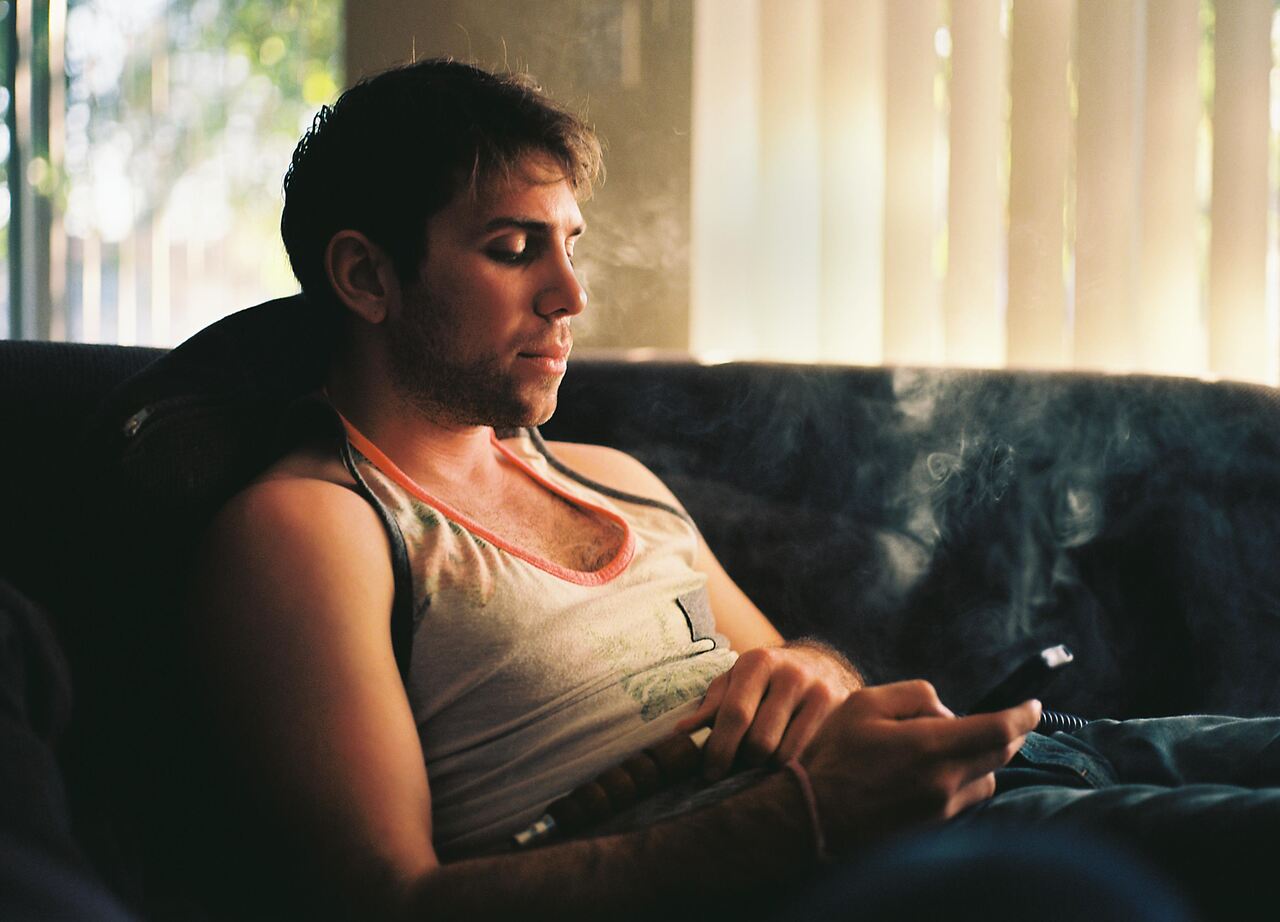 A man is lying on a couch, sending a text message to a woman while holding his phone